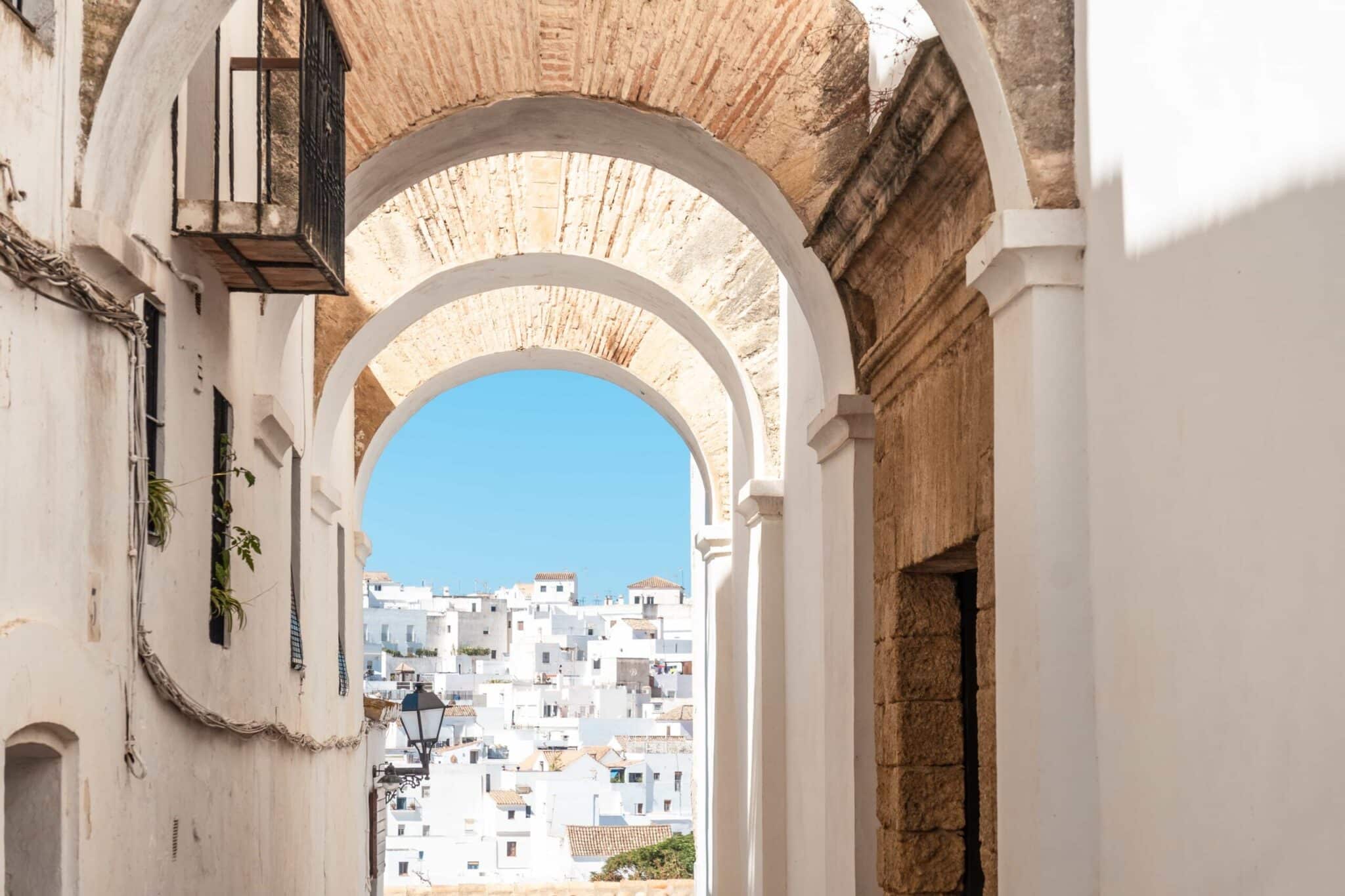 Gewölbter Durchgang in einer weißen Stadt mit Blick auf weiße Häuser im Hintergrund unter klarem blauem Himmel.